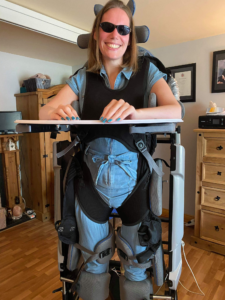 A person with a disability is reclining in a motorized wheelchair in their living room. The wheelchair has a headrest and footrests