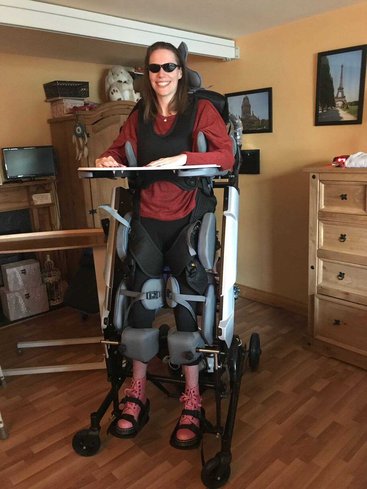 A person with a disability is reclining in a motorized wheelchair in their living room. The wheelchair has a headrest and footrests